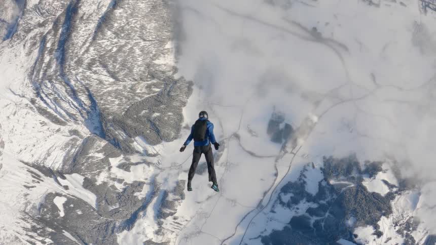 A person skydiving over snowy mountains and forests