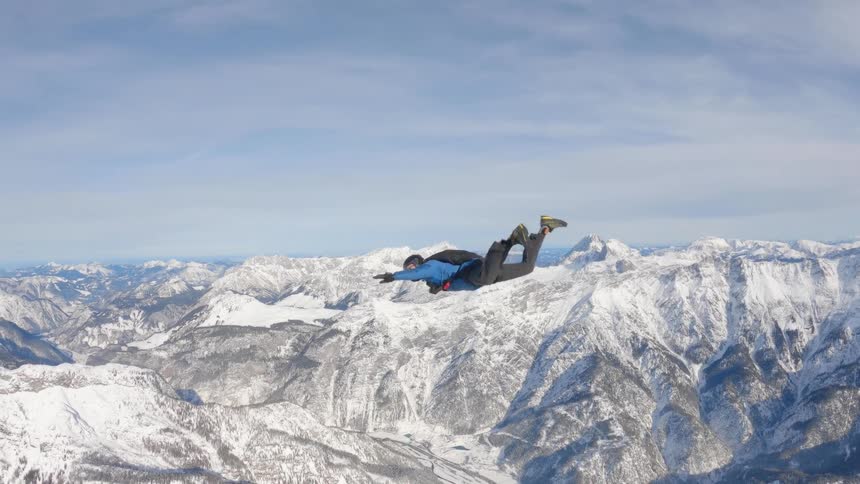 Skydiver wearing a parachute pack and black helmet is floating over a snow covered mountain canyon