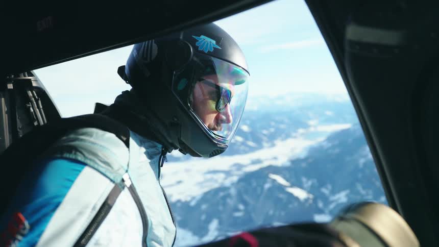 A skydiver taps his chest with his arm as he prepares to jump over a mountain range