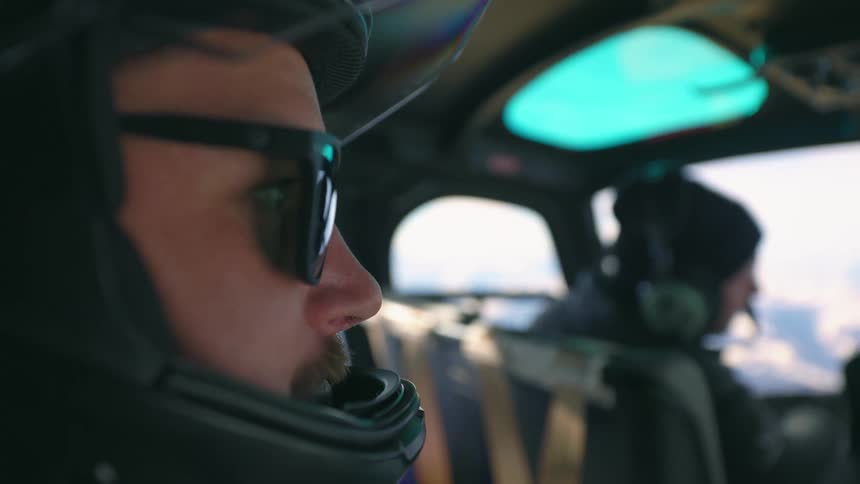 A man wearing a crash helmet and a pair of black sunglasses sitting inside of a moving helicopter