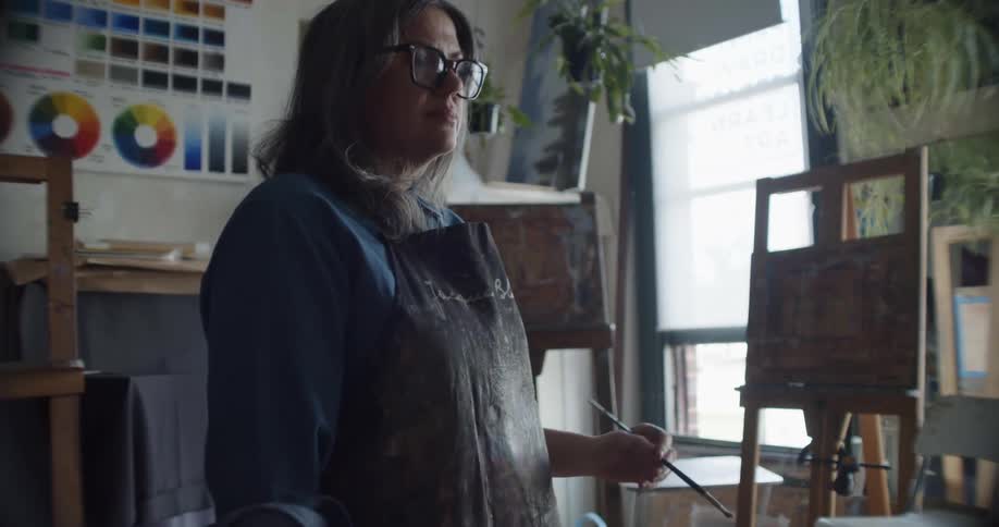 An artist steps back and looks at her canvas after adding brush strokes