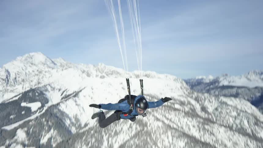 A man skydiving above the mountains pulls the cord on his backpack to release the chute