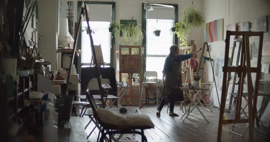 A woman painting looks at her work and wipes it with a cloth