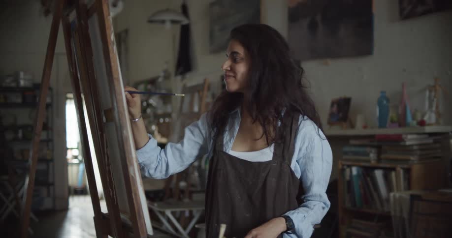 A young woman painting on a canvas in an art studio and smiling at her work