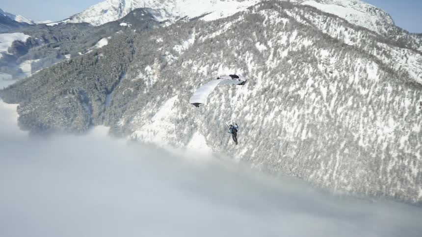 Paraglider floating over fog across snow capped mountains