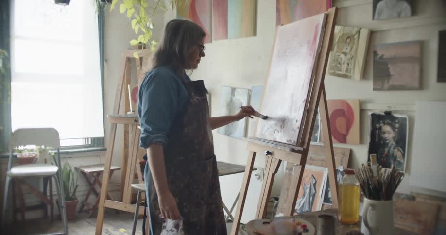 A woman with glasses painting on a canvas with a paintbrush