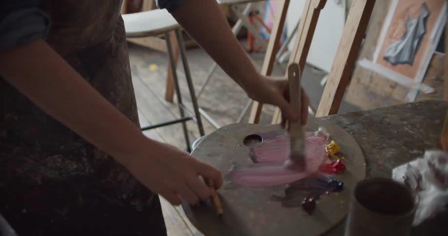 An artist mixing paint on a palette in an art studio
