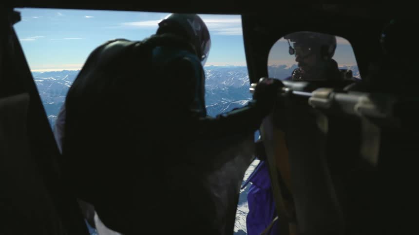 Skydiver wearing a wingsuit readies to jump out of a helicopter over the snow covered mountains