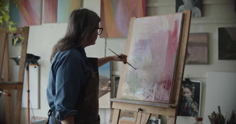 A woman with glasses painting on a canvas with a paint brush