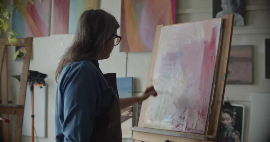 Woman wearing an apron painting with a small brush over canvas in her studio