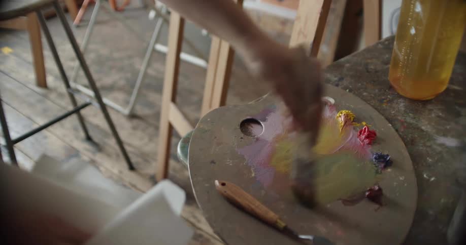 A person using a brush to mix paint on a palette in an art studio