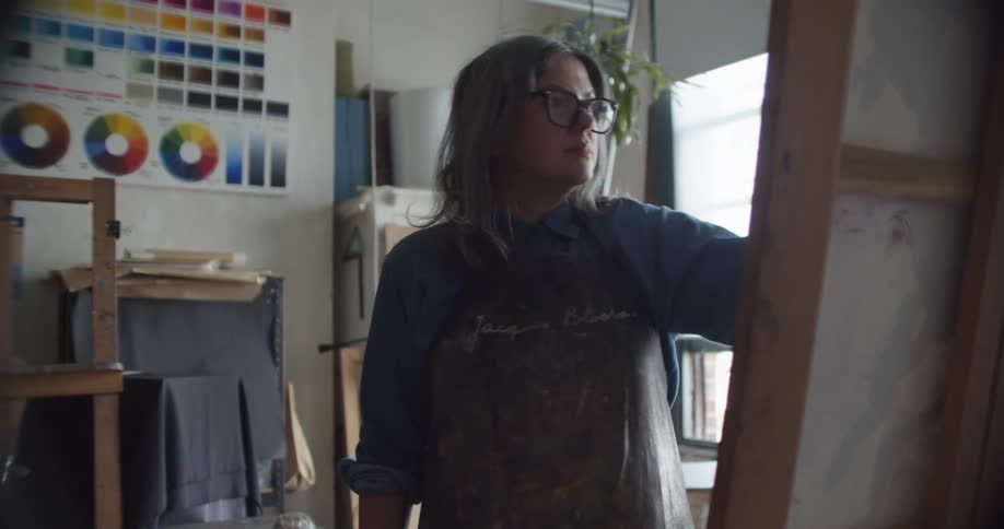 A woman with glasses painting on a canvas with a paint brush