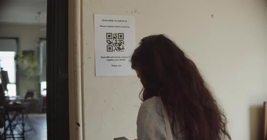 A woman takes a picture of a qr code on a piece of paper on a wall with her smartphone and then walks into a room