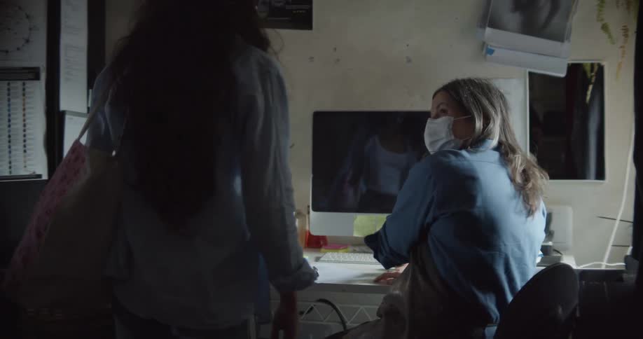 A woman sits at her desk and an employee comes in to have her temperature taken and then walks out