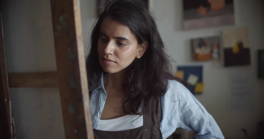 A female artist deep in thought while painting on a canvas in an art studio