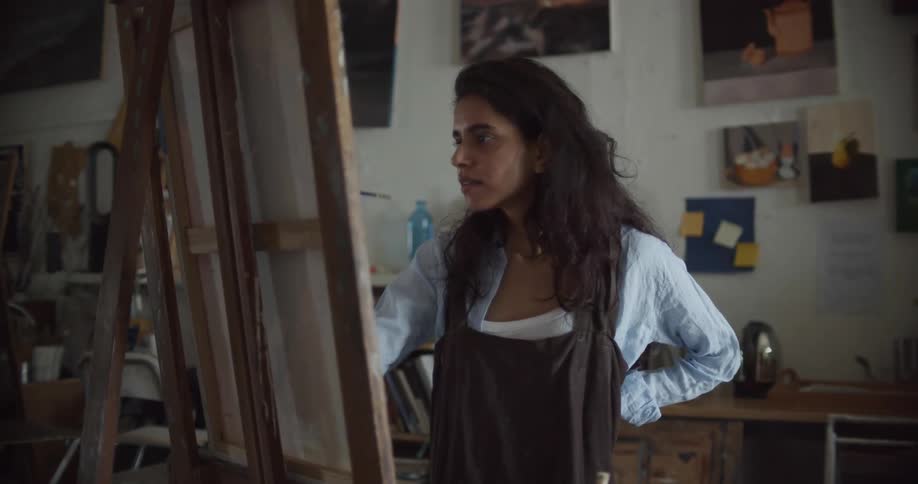 A woman uses a pencil to sketch a drawing onto an easel in an art studio during the day