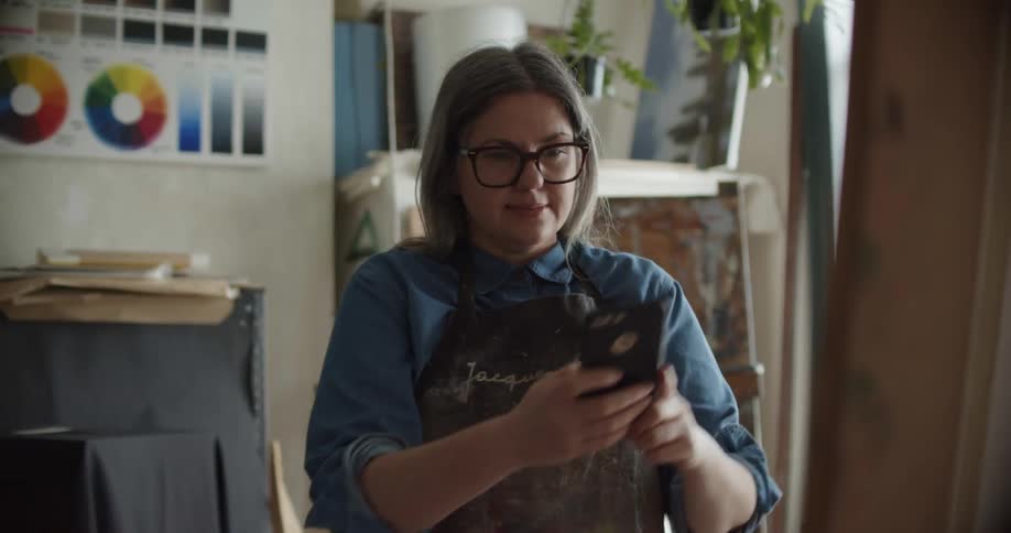 A woman taking a photo of something she painted with a cell phone