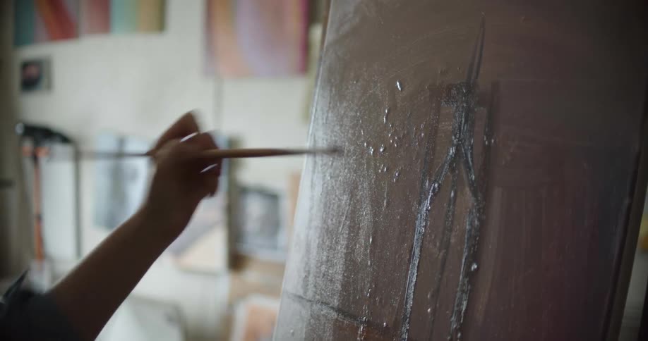 A woman with glasses and an apron painting on a canvas with a paint brush