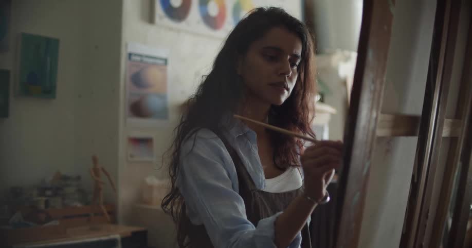 An artist paints on a canvas before standing back to examine her work