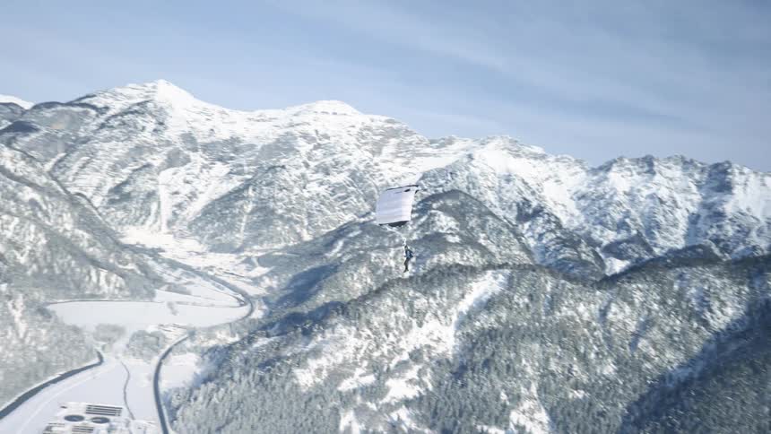 A person paragliding with a mountain range the sky and clouds in the background