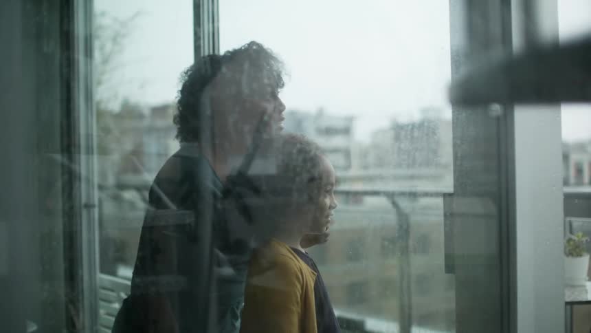 A woman and her daughter gaze through a large window at the cityscape on the other side