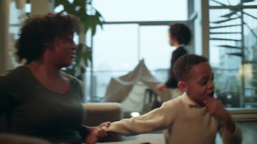 A boy hugs his mother as their family sits on a living room couch in their downtown loft