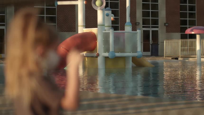 A young girl stands at a fence and looks at a flooded playground at a school