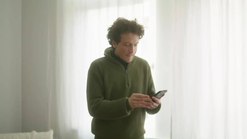 A man looks worried as he looks at his phone and runs his hand through his hair and then makes a phone call and smiles and talks