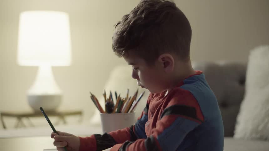 Little boy coloring with colored pencils on coffee table in living room