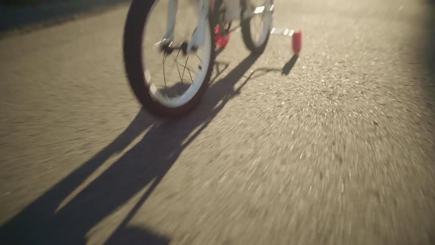 A child riding a bike with training wheels down the road