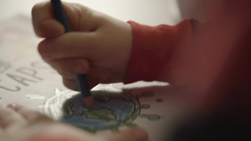 A child colors in a picture of the planet earth with a blue colored pencil
