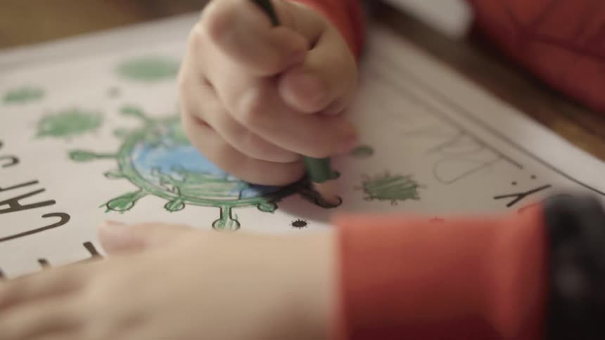 A child colors a small poster with a green colored pencil