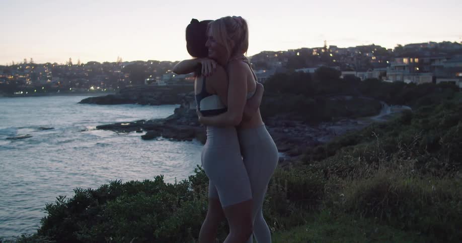 Two women hugging on a shore by a neighborhood smile and laugh