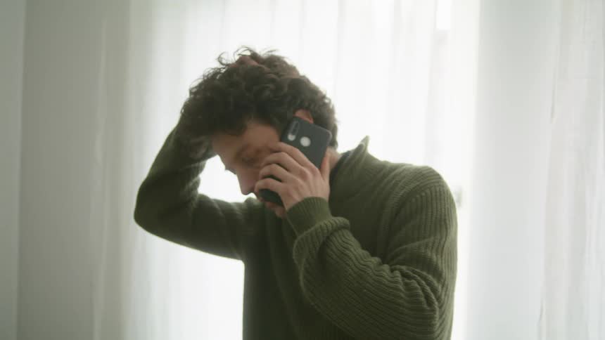 A man shakes his head and runs his hand through his hair as he talks on the phone
