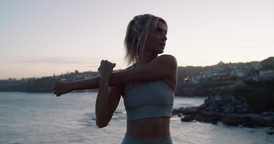 Young fit woman wearing sports clothes working out near the ocean at morning