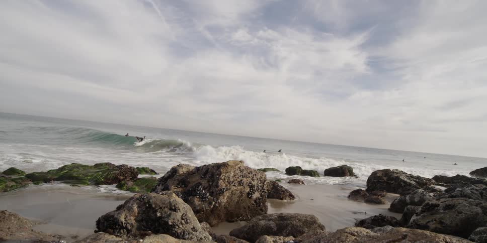 Surfers are riding waves towards the shore with many rocks nearby
