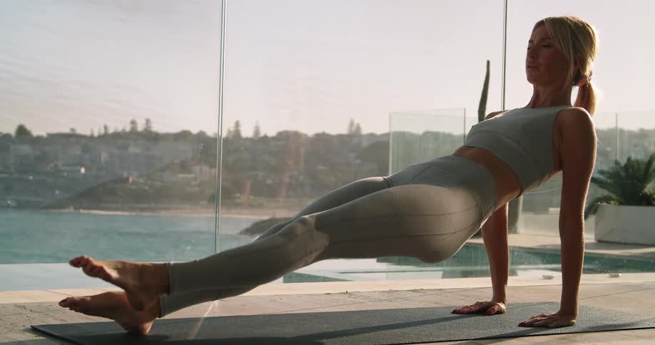 A young woman performs a leg exercise while on a patio overlooking a scenic coastal locale