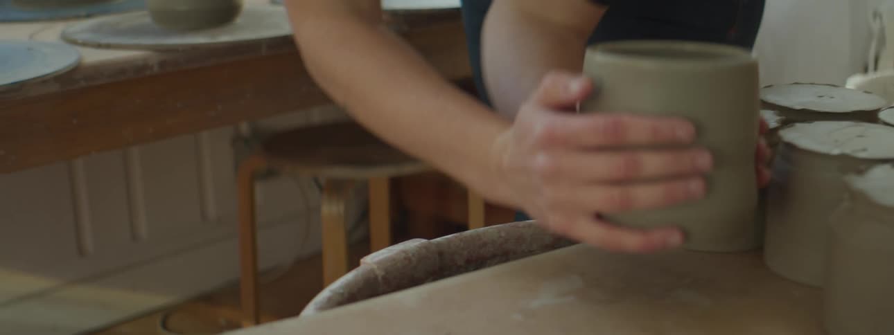 A woman moves freshly made pottery from a large table to a small side table