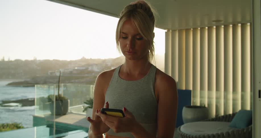 A woman in her home on the shore scrolls on her cell phone