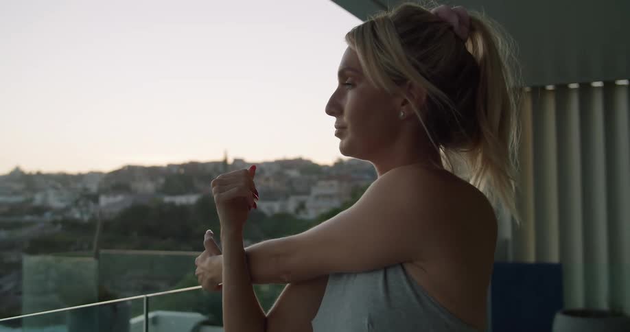 A woman in a sports bra stretching her arm on a balcony