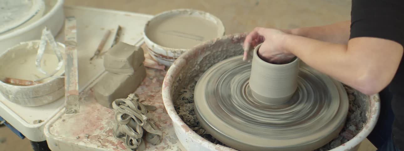 A woman shaping a piece of clay on a pottery wheel inside of an art studio
