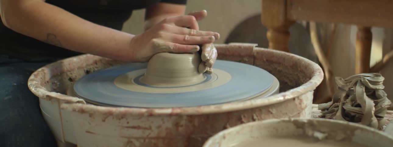 A person is making clay pottery while sitting indoors