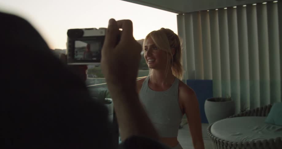 A man takes a picture of a woman smiling at a camera while standing on a patio in a beach house