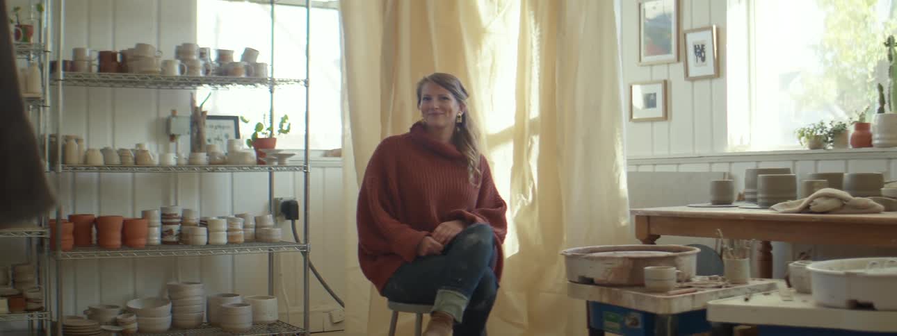 A woman sits in her ceramics shop and smiles