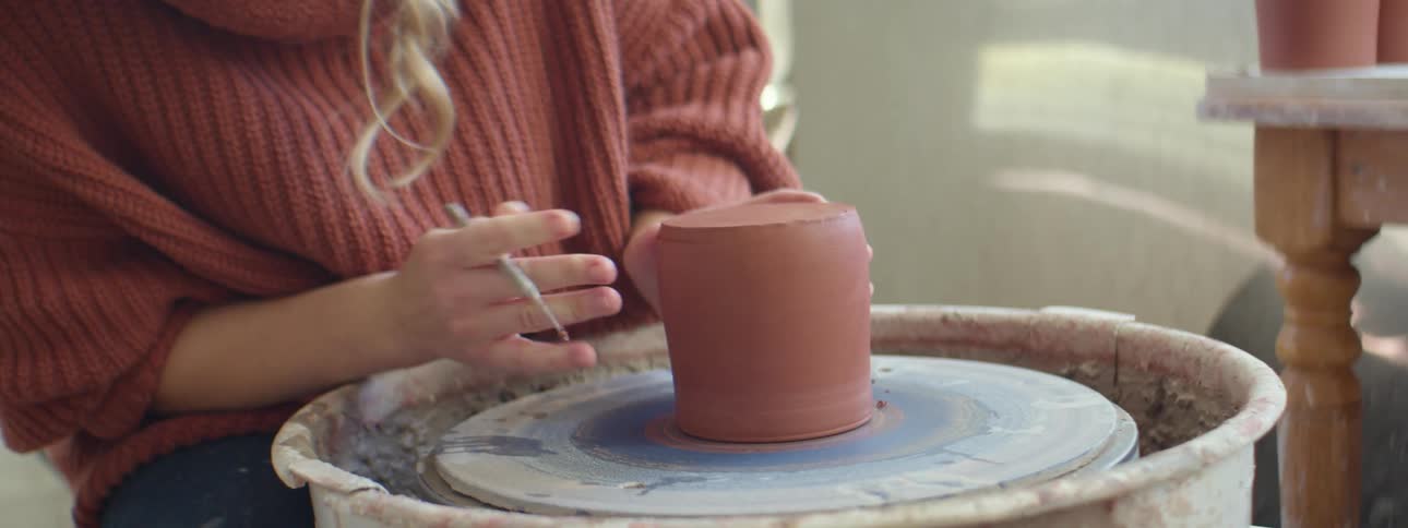 A woman sitting at a pottery wheel sculpting clay with a tool