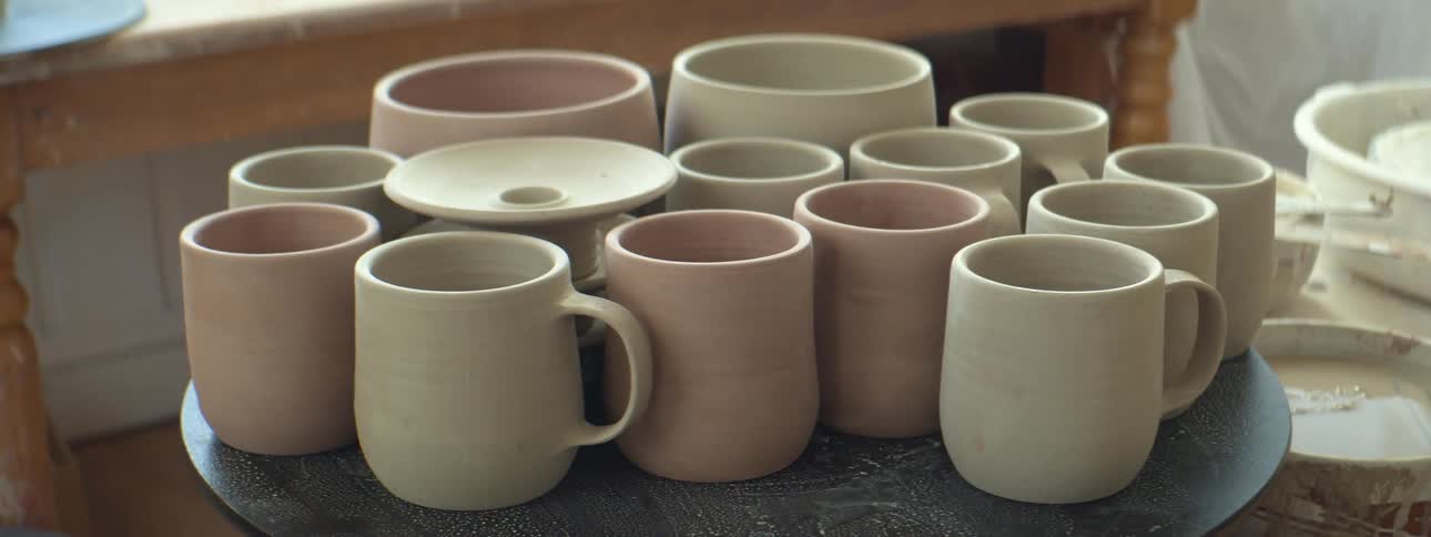 Pink and white ceramic mugs and pots on a table inside of a workshop
