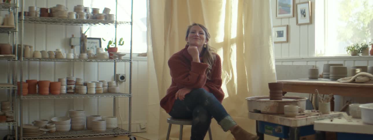 A woman in a room sitting on a chair with windows and shelves in the background