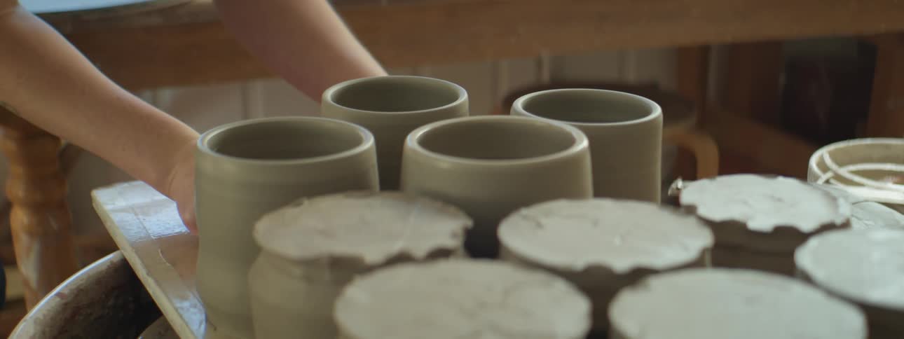 A person placing clay cups onto a table in a pottery studio