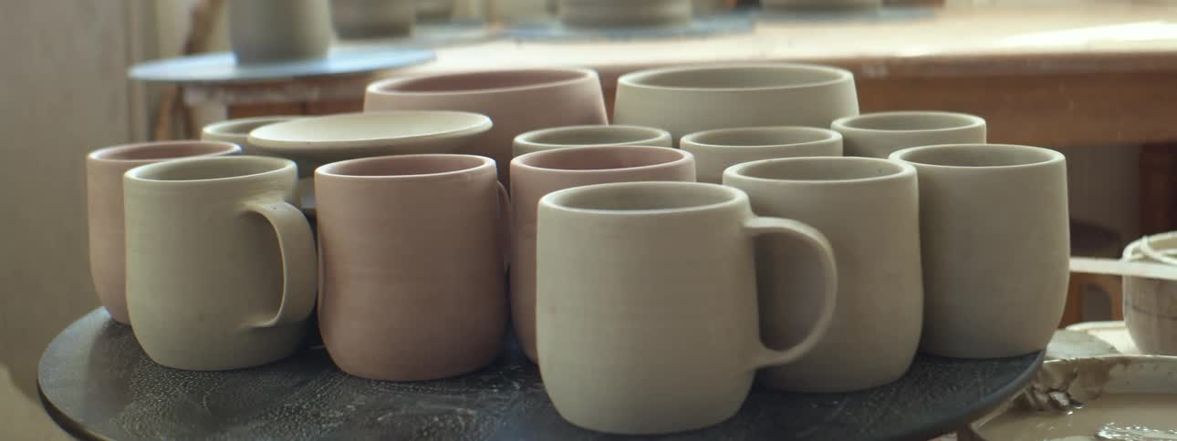 Beige and pink ceramic mugs on top of a small table in a workshop at daytime