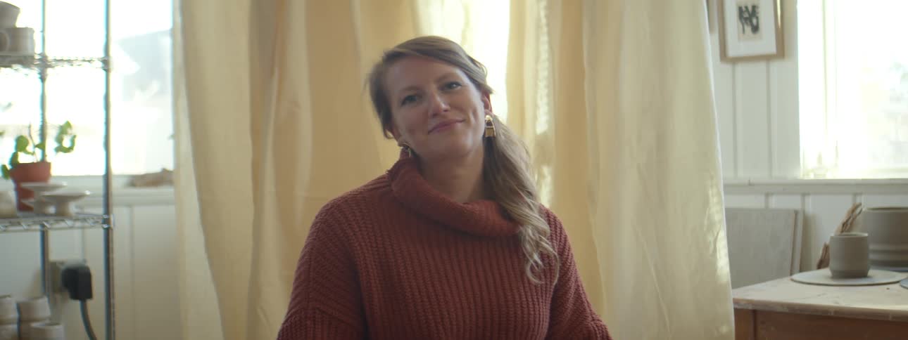 A woman sitting inside of a room in a house smiling at the camera during the day